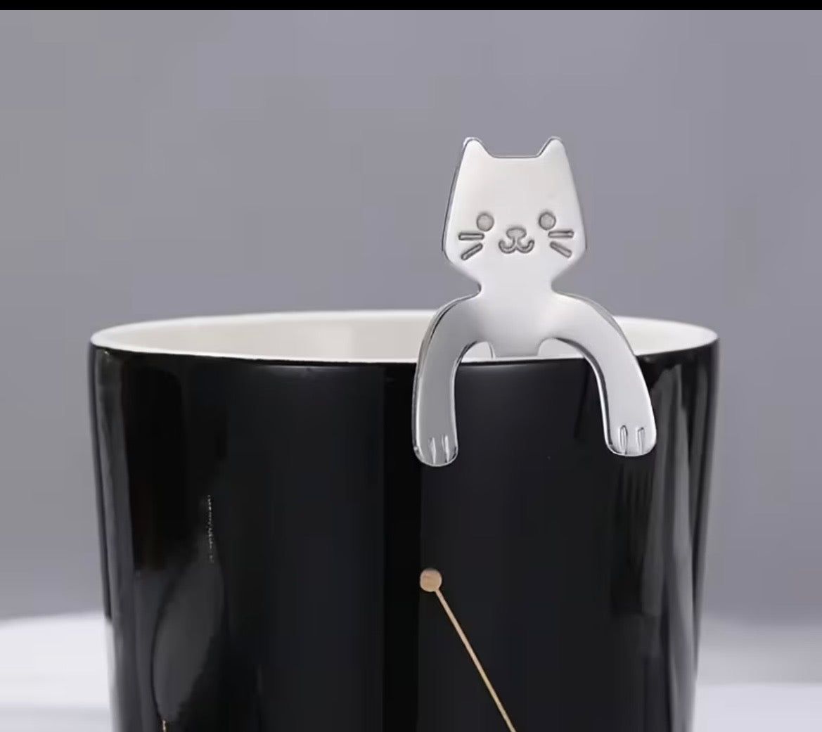 Cat-shaped spoon holder on a black mug with a gray background