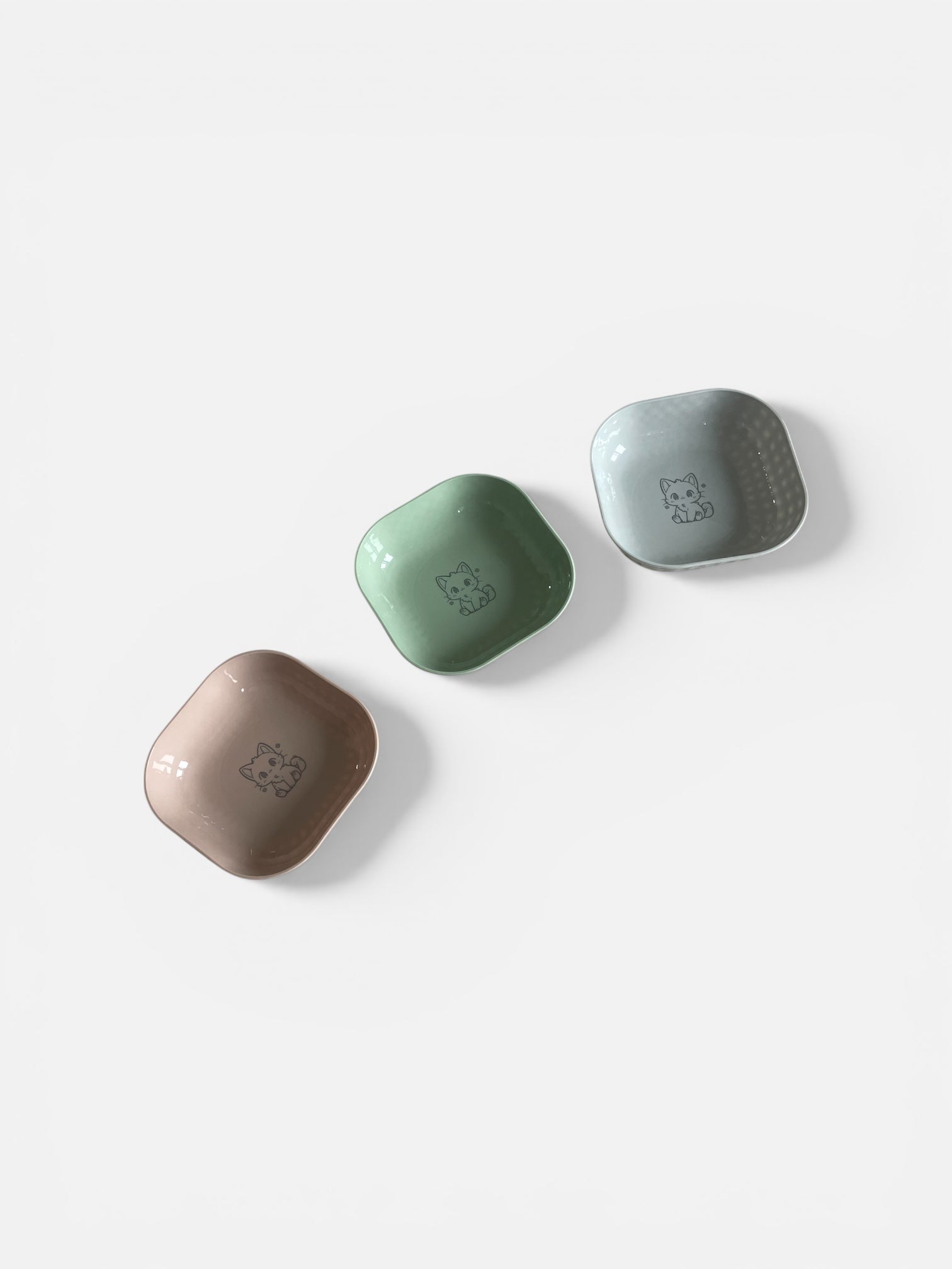 Three ceramic bowls in green, beige, and gray on a white background
