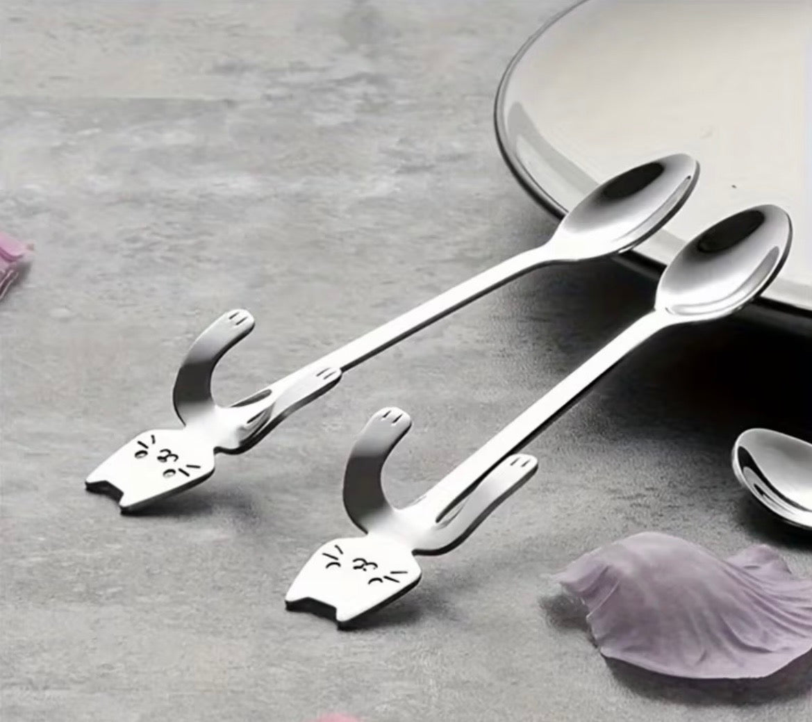 Three cat-shaped spoons on a gray surface with a blurred background