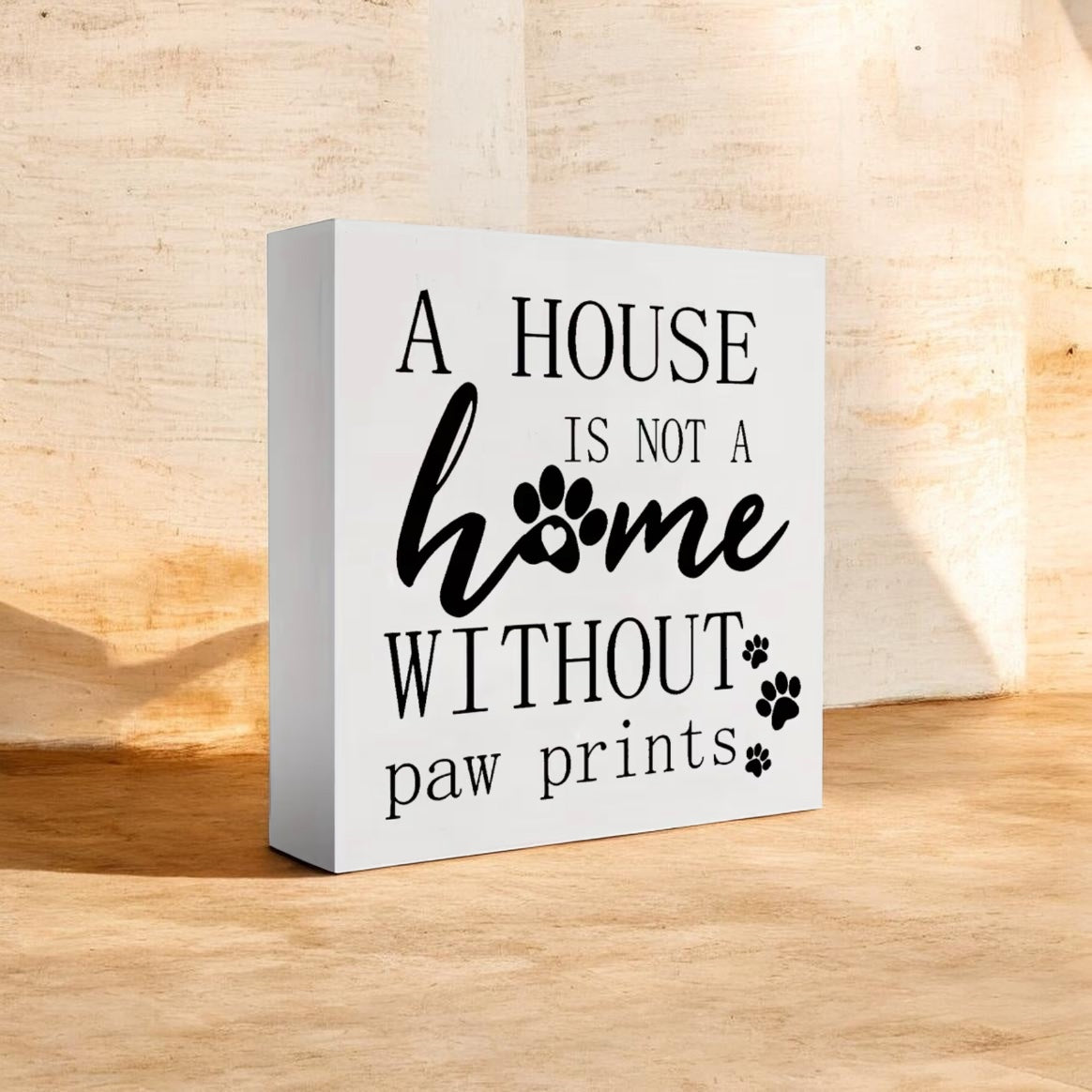 Decorative sign with text 'A house is not a home without paw prints' on a wooden surface.