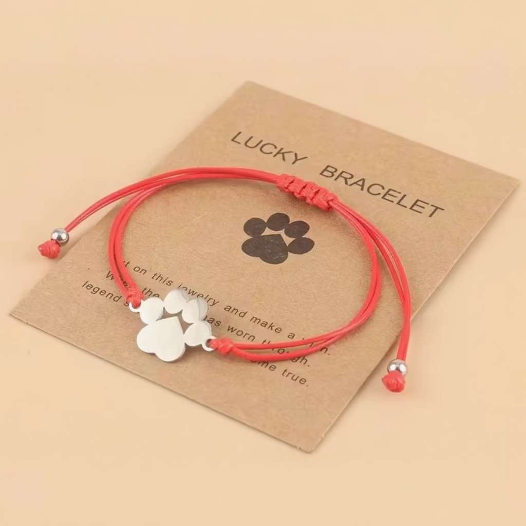 Red bracelet with paw charm on a brown card labeled 'Lucky Bracelet' on a beige background