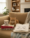 Cat sitting on a couch with books and a t-shirt featuring a cat design.